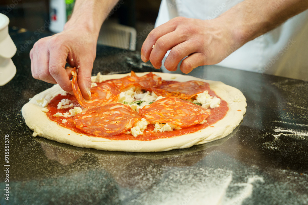 A chef preparing a pizza with tomato sauce and mozzarella cheese, spreading salami on pizza A chef preparing a pizza with tomato sauce and mozzarella cheese, spreading salami on pizza