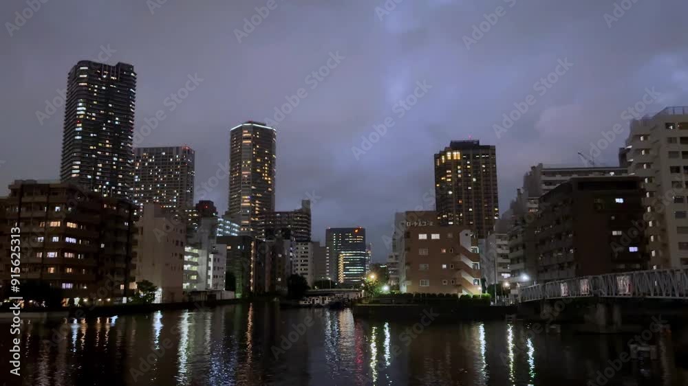 Nighttime view of Tokyo's Harumi district skyline with thunderclouds and city lights reflected on water Nighttime view of Tokyo's Harumi district skyline with thunderclouds and city lights reflected on water