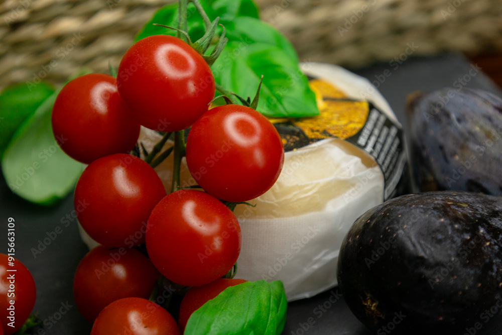 A head of cheese with a juicy branch of cherry tomatoes, green aromatic basil and purple figs on a gray background. Copy space the text. Banner. A head of cheese with a juicy branch of cherry tomatoes, green aromatic basil and purple figs on a gray background. Copy space the text. Banner.
