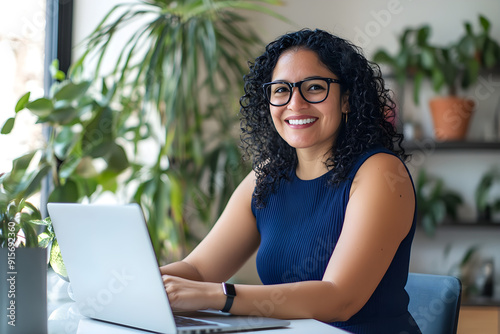 Beautiful Woman with Curly Black Hair, Spectacles, and a Nice Smile, Wearing a Sleeveless Blue Top and Working on a Laptop