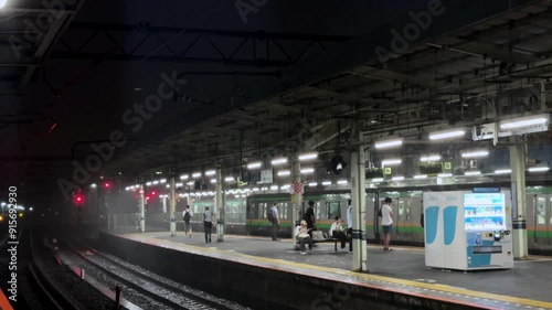 Commuters wait on a platform at Tokyo's Shinagawa Station at night with lights illuminating the scene