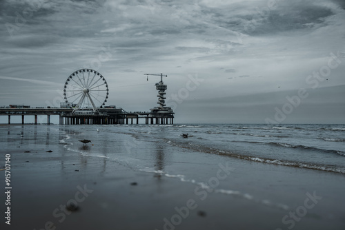Moody seaside scene featuring a ferris wheel and pier extending into the ocean under an overcast sky, with reflections shimmering on the wet sand