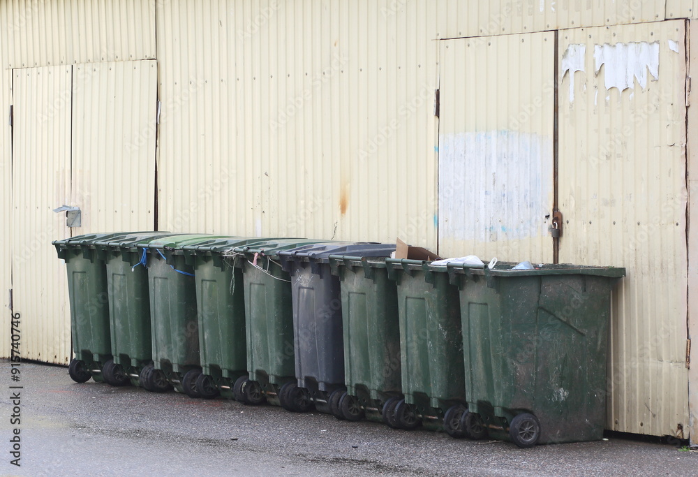 Mobile dumpsters on wheels stand in a row near the wall of the hangar