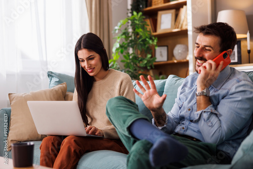 Woman working using laptop computer while man having phone conversation at home