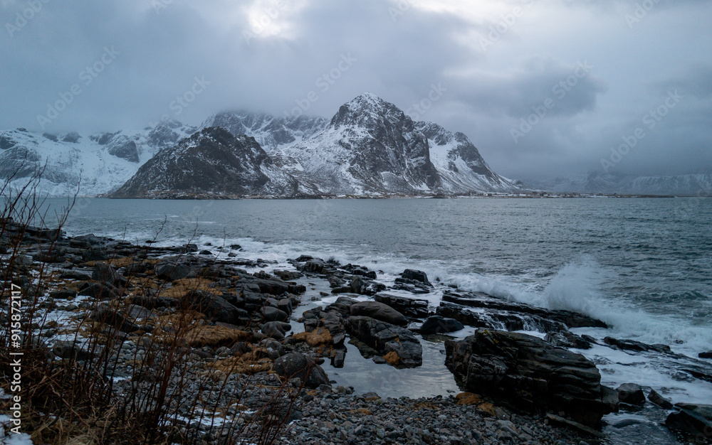 A scenic coastal view featuring a snow-capped mountain, rocky beach, stormy sky, and dynamic ocean, Lofoten, Norway A scenic coastal view featuring a snow-capped mountain, rocky beach, stormy sky, and dynamic ocean, Lofoten, Norway