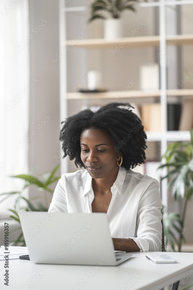 Focused woman with afro hairstyle working on laptop in modern home office. Concepts of remote work, concentration, and productivity. Focused woman with afro hairstyle working on laptop in modern home office. Concepts of remote work, concentration, and productivity.