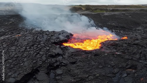 Chunks of hardened lava fall away from the cooling surface revealing pockets of molten rock and steam underneath. photo