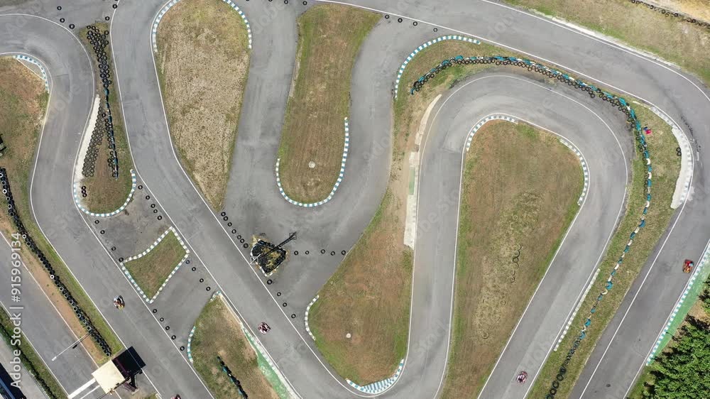 Aerial drone view of go-kart track with several karts racing along the winding course. Dynamic scene capturing speed and excitement of kart racing from above