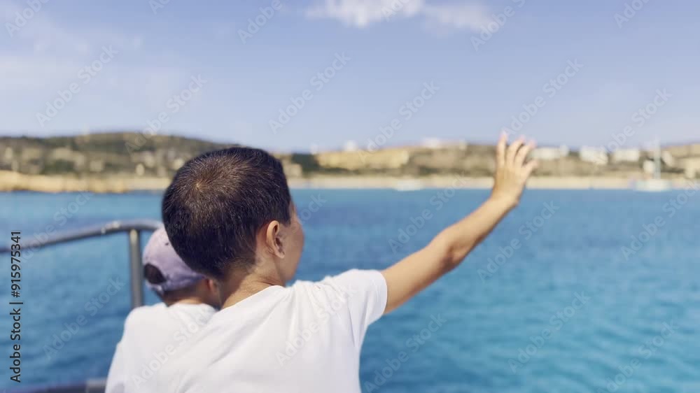 A cheerful boy waves happily while aboard a boat, enjoying a sunny day and the vibrant blue waters around him. A cheerful boy waves happily while aboard a boat, enjoying a sunny day and the vibrant blue waters around him.