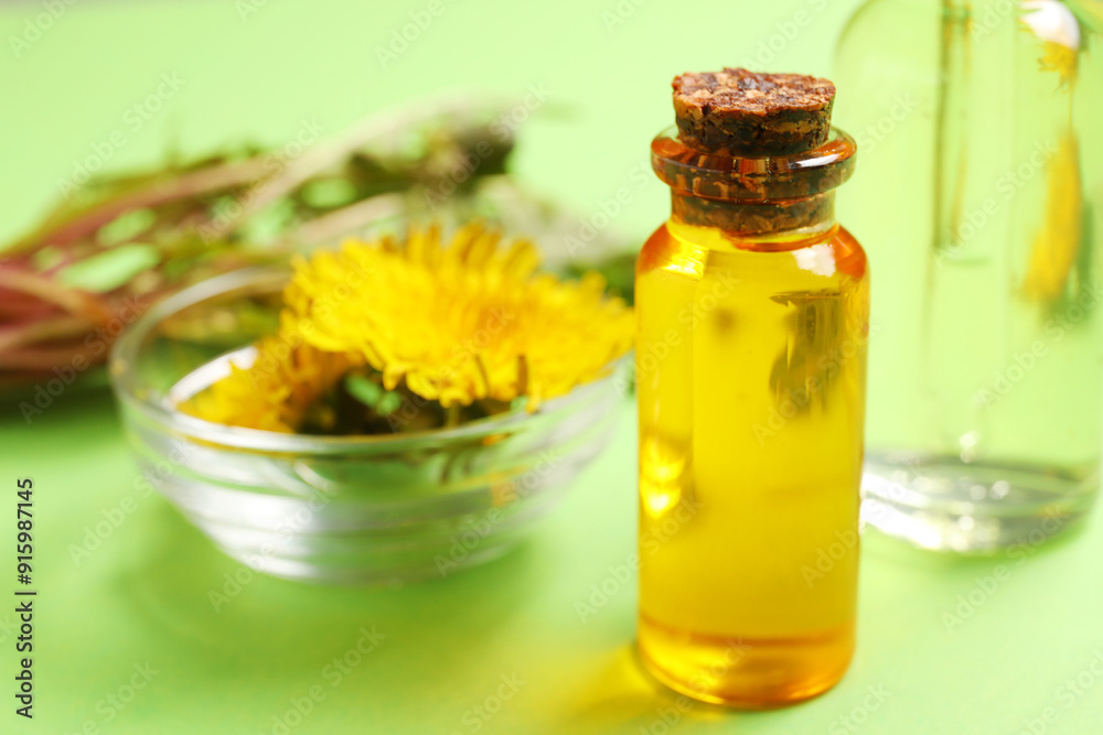 Bottles with cosmetic oil and bowl of dandelion flowers on green background Bottles with cosmetic oil and bowl of dandelion flowers on green background
