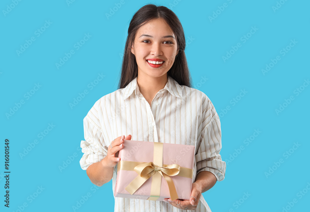 Beautiful young Asian woman with gift box on blue background Beautiful young Asian woman with gift box on blue background