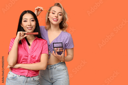 Pretty young women with decorative cosmetic products on orange background