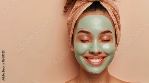 Satisfied young woman applying a clay face mask, achieving smooth and fresh skin, on a beige background