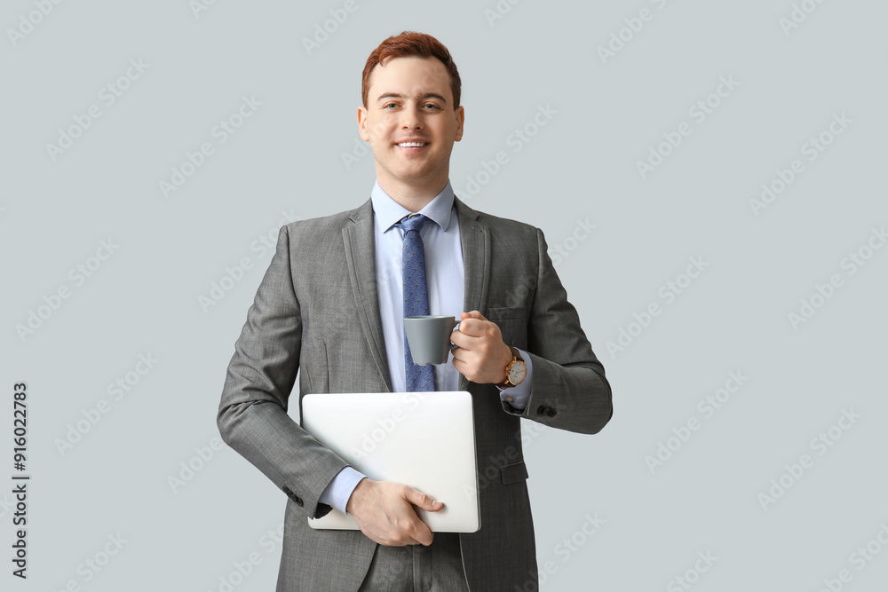 Young man holding cup of fresh coffee and laptop on grey background Young man holding cup of fresh coffee and laptop on grey background