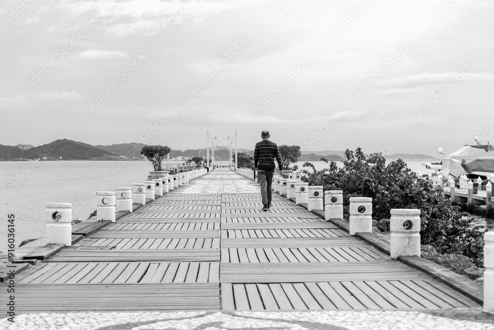 Obraz premium Homeme caminhando sozinha no mole da barra sul de Balneário Camboriú, fine art