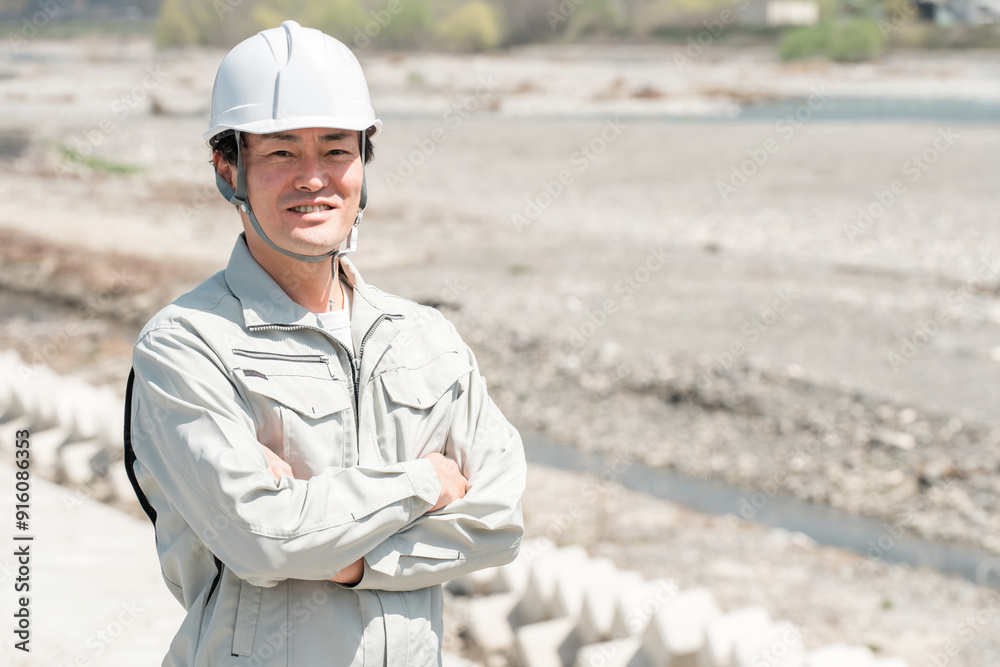 土木業・河川工事・建設現場に立つヘルメットを被った作業着姿のアジア人男性作業員
土木業・河川工事・建設現場に立つヘルメットを被った作業着姿のアジア人男性作業員