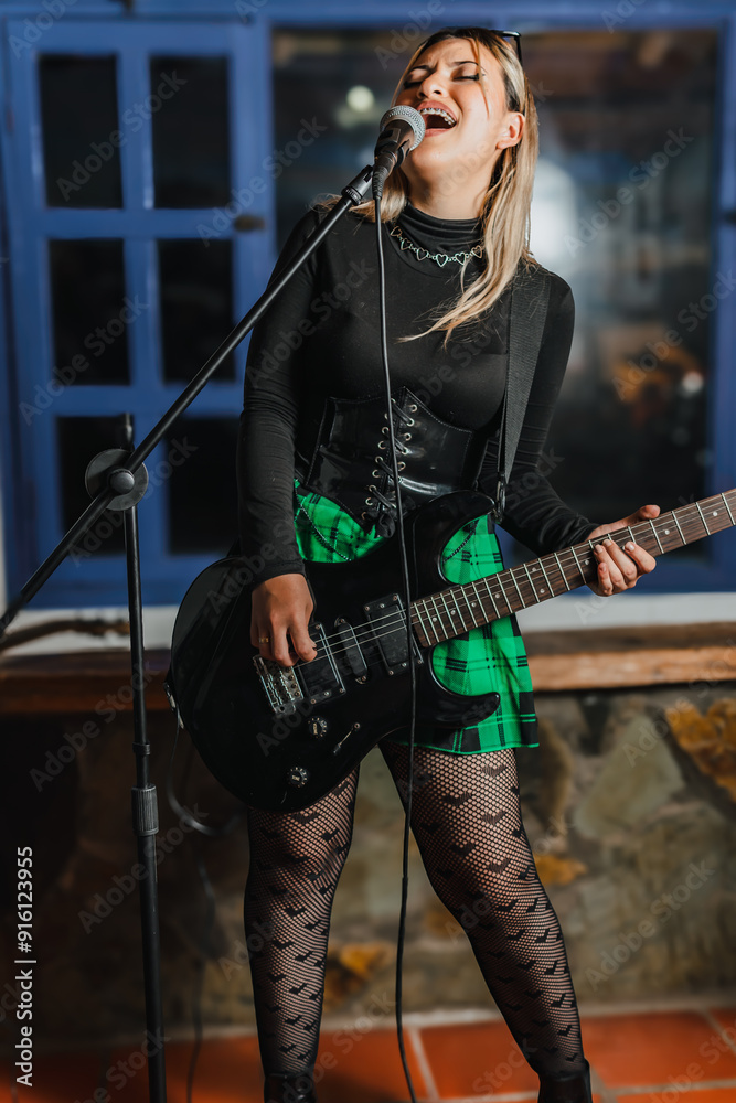 Obraz premium Woman singer playing bass guitar. Band rehearsing at home. International music day.