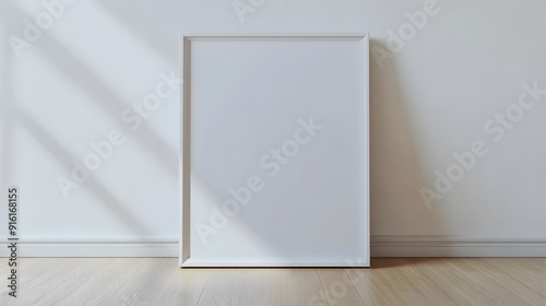 White frame with a blank poster leaning against a plain white wall on a light wooden floor