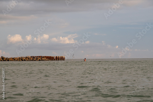 Distant view of a shirtless man standing in ocean fishing at sunset, Sunset Beach, Treasure Island, Florida, USA photo