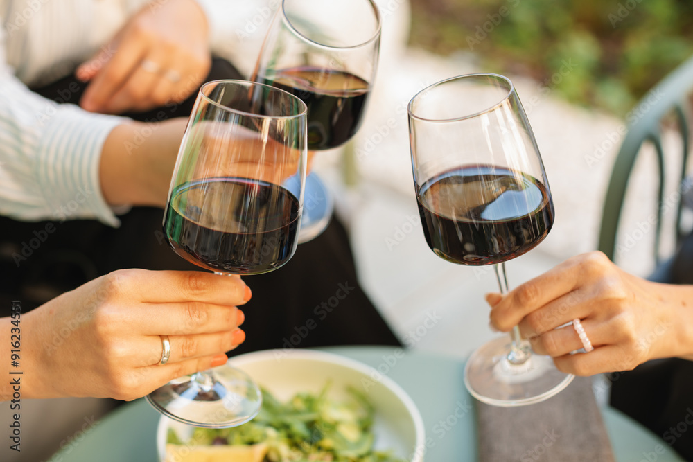 Close-up of three woman clinking glasses of red wine while relaxing on the summer terrace Close-up of three woman clinking glasses of red wine while relaxing on the summer terrace