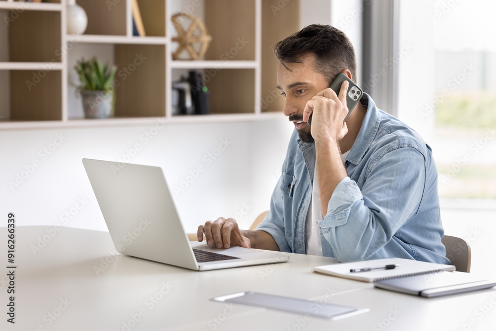 Focused handsome Latin businessman talking on mobile phone at laptop, using wireless Internet technology for job communication, giving consultation to customer on telephone Focused handsome Latin businessman talking on mobile phone at laptop, using wireless Internet technology for job communication, giving consultation to customer on telephone