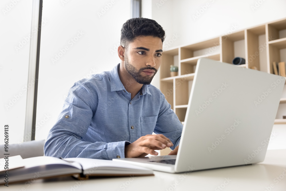 Focused serious young Arab employee man in casual typing on laptop, working in office, sitting at workplace table, browsing business social network, chatting on professional app, service Focused serious young Arab employee man in casual typing on laptop, working in office, sitting at workplace table, browsing business social network, chatting on professional app, service
