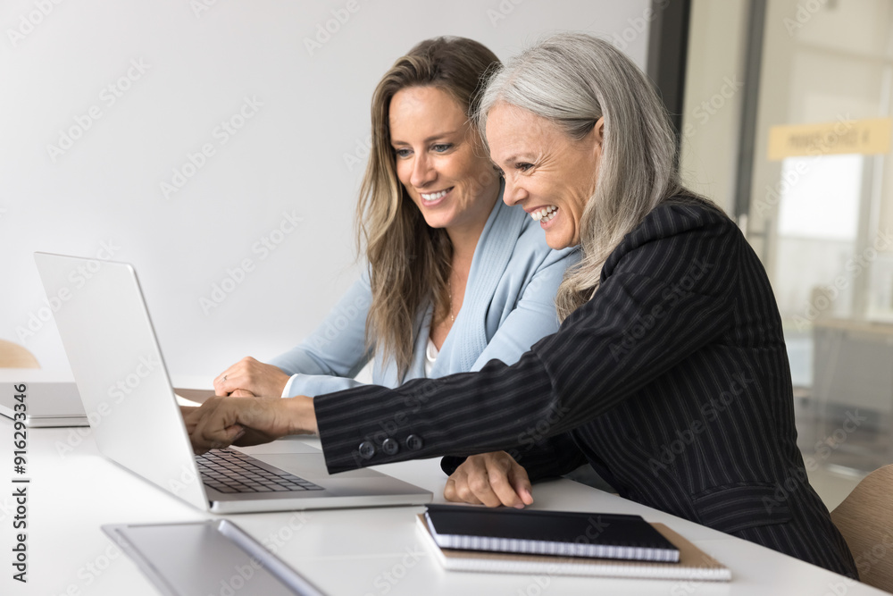 Happy different aged female business colleagues looking and pointing at laptop screen, laughing, getting good news, enjoying online business communication, teamwork, working together on project Happy different aged female business colleagues looking and pointing at laptop screen, laughing, getting good news, enjoying online business communication, teamwork, working together on project
