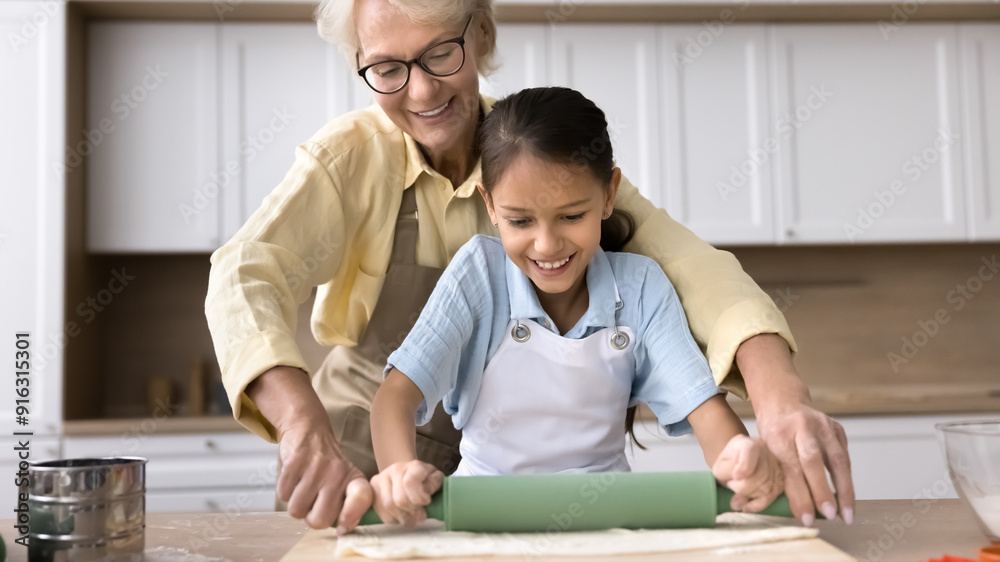 Obraz premium Joyful blonde granny helping cute grandkid girl to roll dough in home kitchen. Happy grandma and granddaughter kid enjoying family culinary baking hobby, preparing bakery food. Banner shot
