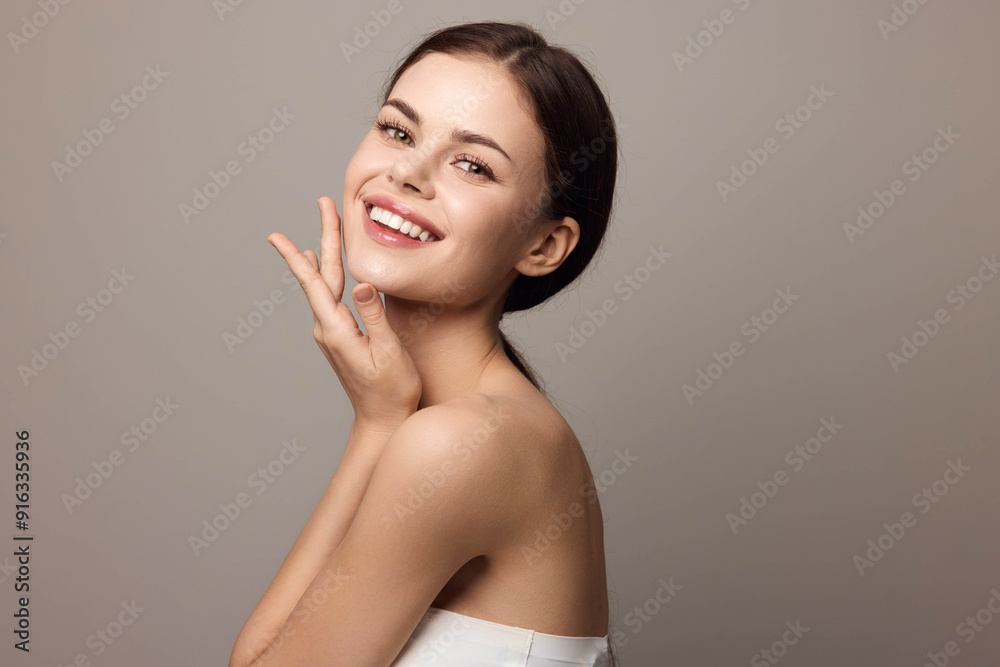 Beautiful young woman with her hands on her face looking at the camera on a gray background Beautiful young woman with her hands on her face looking at the camera on a gray background