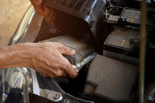 A close-up image of a person’s hands removing a used air filter from a car’s engine compartment.