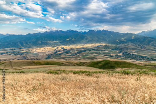 Panoramic view of mountain range and fields in mountain valley. Dramatic stormy sky. Mountain landscapes of Kyrgyzstan.