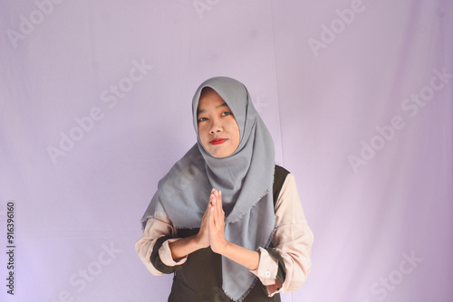 Portrait of smiling beautiful young Asian Muslim woman wearing hijab standing with Eid greeting gesture and welcoming Ramadan isolated on white studio background