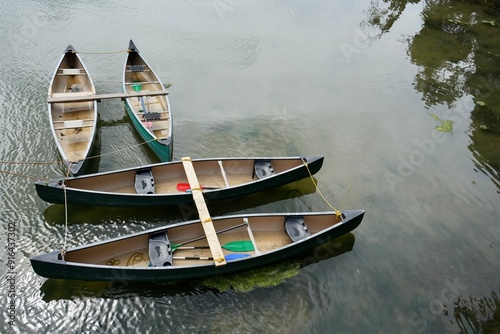 4 empty canoes tied up on a calm river with trees reflected in the water. photo