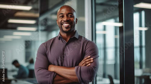 Portrait of a smiling black businessman standing with his arms crossed in a modern office and looking away, his team working on a whiteboard behind him. 