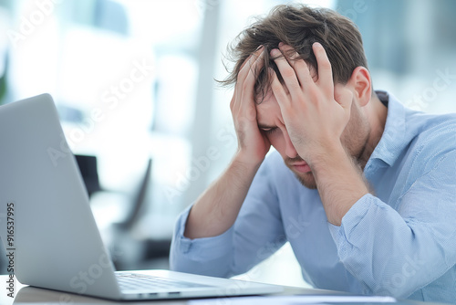 Wallpaper Mural A stressed man with his hands on his head, sitting in front of a laptop in a brightly lit office, expressing frustration and work-related stress. Torontodigital.ca