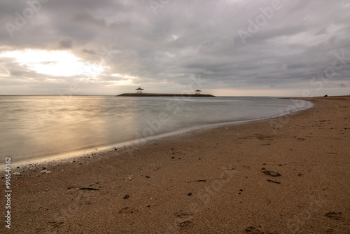 Beautiful seascape in the morning. Tropical sandy beach with breakwater and reflection of the sky in the calm water. Sanur, Bali, Indonesia