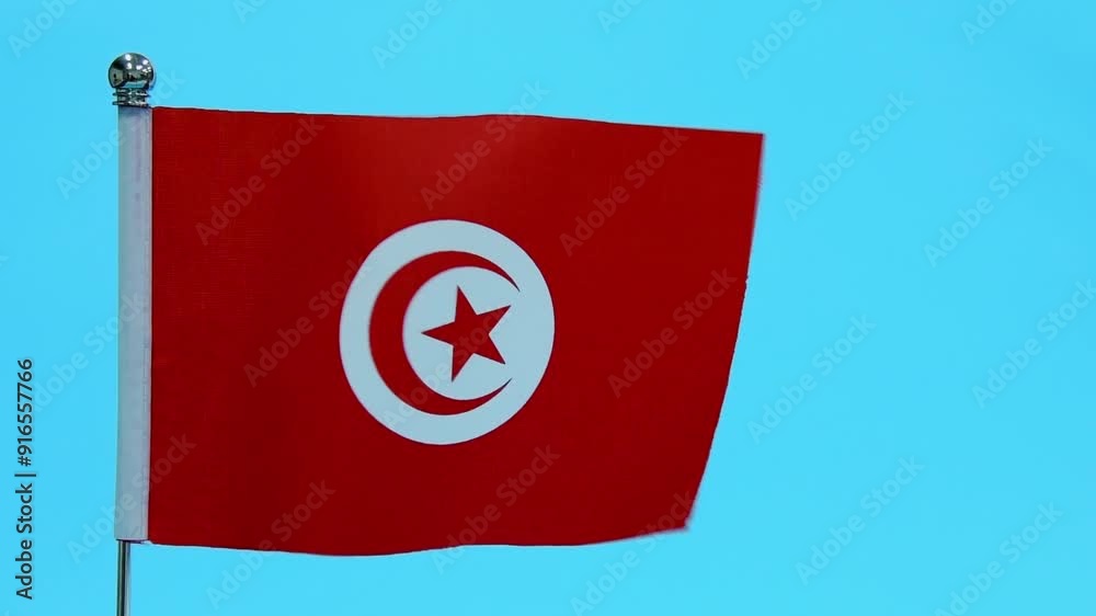 Slow motion video of Tunisian table flag waving on blue background Slow motion video of Tunisian table flag waving on blue background
