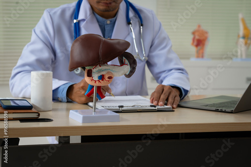 Fotografie A male doctor sits at a table in a liver disease clinic, giving online advice on hepatitis A, D, E, pancreatitis, fatty liver, cirrhosis, liver cancer, and pancreatic cancer