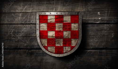 Medieval wooden shield with silver brim and red checkered pattern design on ancient wooden background