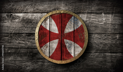 Medieval round wooden shield with golden brim and cicular templar red white  pattern design on ancient wooden background