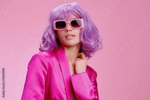 Purplehaired woman in sunglasses and a pink suit, posing confidently against a matching pink background, exuding a bold and stylish fashion statement with her unique and vibrant appearance