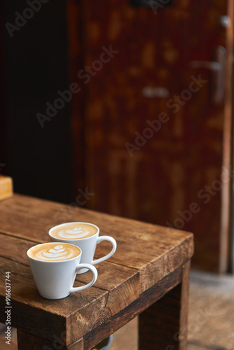 Two cups of hot coffee with milk on a wooden table outside