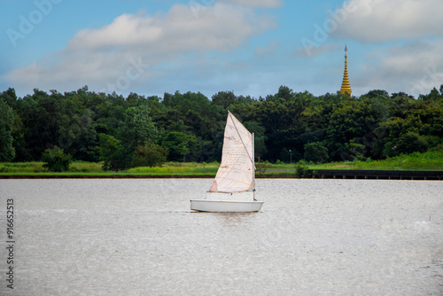 A small white sailboat floating in the middle of the water in a park during a nice summer.
