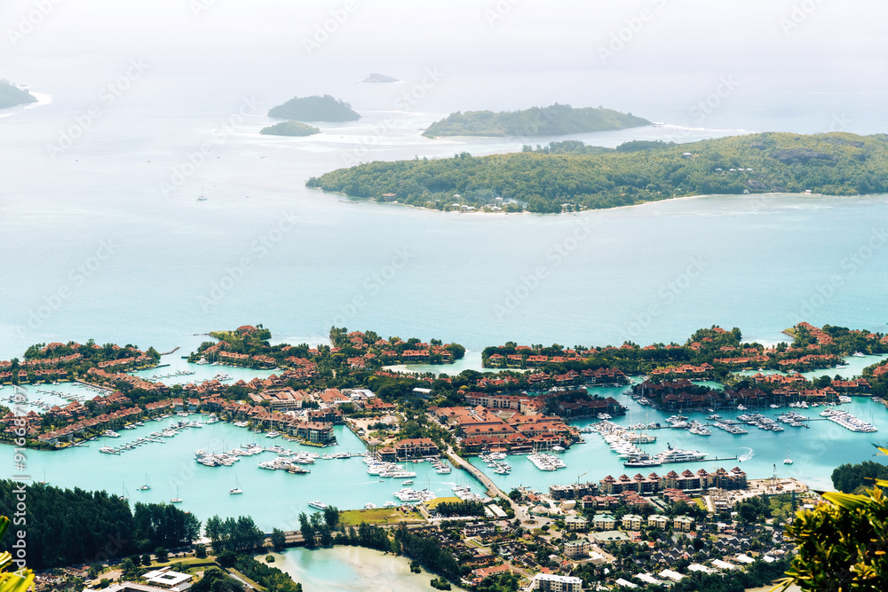 Fototapeta premium A stunning aerial view of a tropical island resort in the Seychelles, featuring a pristine marina filled with yachts and surrounded by lush vegetation