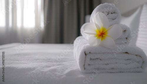 Flower on stack of white towels on bed in light