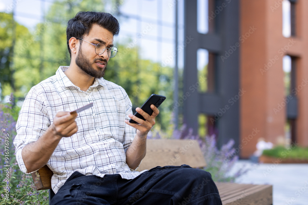 Fototapeta premium Man holding credit card and smartphone, concerned about possible fraud, sitting outdoors
