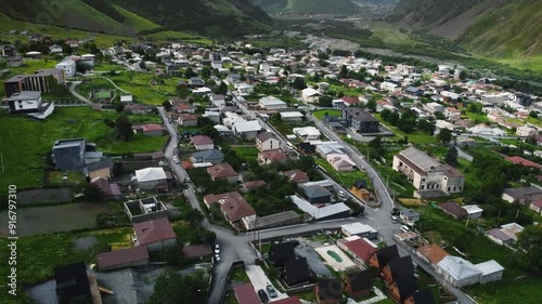 aerial shot forward camera lift view of the village of kazbegi georgia with a view of the mountain valley with summer greenery cinematic shot with a view of the mountains and a small town