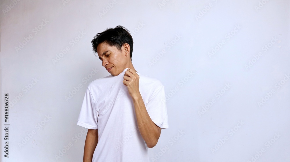 Young Asian man wearing white shirt gesture smelling bad smell from his shirt isolated white background Young Asian man wearing white shirt gesture smelling bad smell from his shirt isolated white background