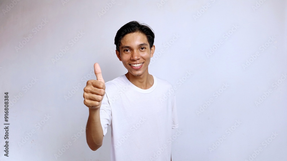 Asian young man wearing white shirt smiling okay gesture using thumbs up Asian young man wearing white shirt smiling okay gesture using thumbs up