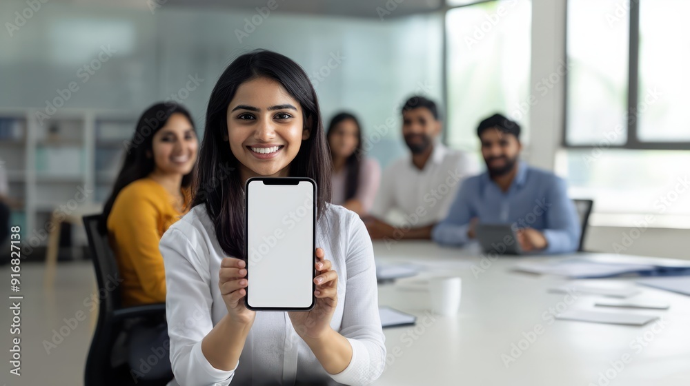 Indian woman holding a phone showing a screen sitting at a work office table, professional setting, workplace, mobile marketing Indian woman holding a phone showing a screen sitting at a work office table, professional setting, workplace, mobile marketing